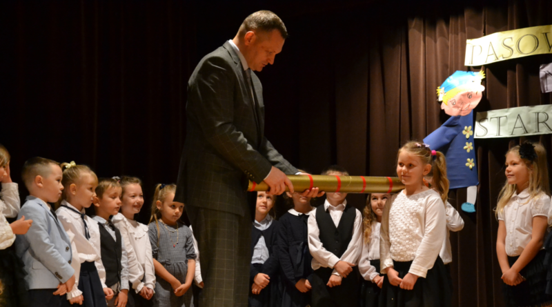 przedszkolaki wraz z burmistrzem, który pasuje dziewczynkę symbolicznym ołówkiem