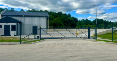 Budynek parterowy w kolorze szarym, ogrodzony bramą.