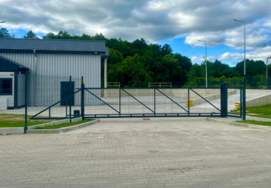 Budynek parterowy w kolorze szarym, ogrodzony bramą.