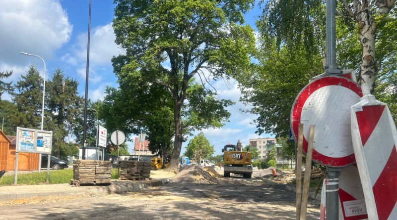 plac budowy - rozkopana ziemia w pasie drogi, z lewej strony duże drzewa, z prawej znaki drogowe informujące o zakazie wjazdu.