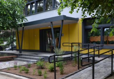 Przedszkole Publiczne w Zawidowie – rekrutacja na rok 2026/2027 Żółty budynek przedszkola pośród drzew. Przed drzwiami frontowymi schody i barierki, obok po prawej stronie podjadę dla niepełnopsrawnych oraz pasaż zieleni.