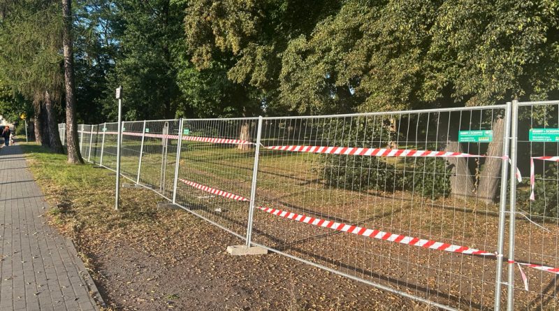 Drzewa ogrodzone siatką, na siatce umieszczone biało-czerowone taśmy budowlane.