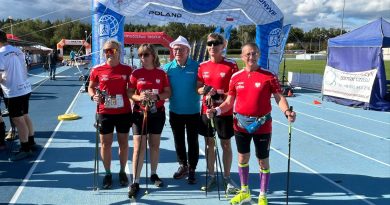 Piecu sportowców na bieżni, ubranych w czerwone koszulki i czarne spodenki. W tle baner organizatora zawodów.