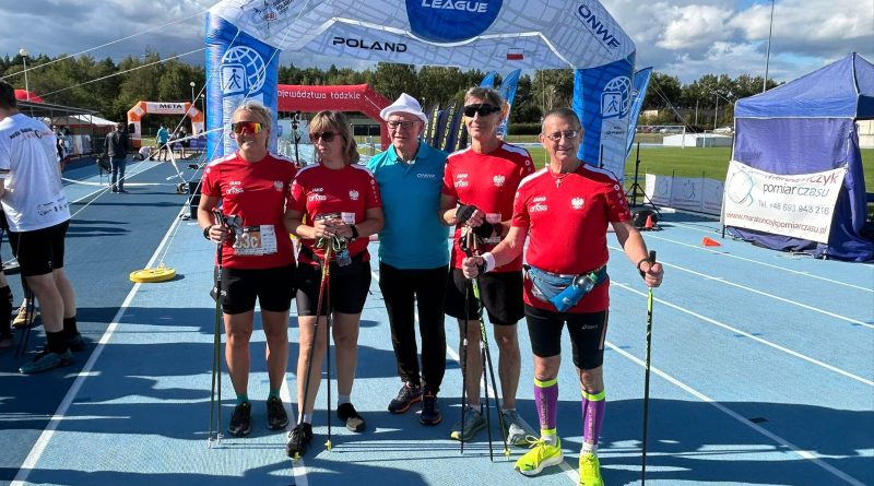 Piecu sportowców na bieżni, ubranych w czerwone koszulki i czarne spodenki. W tle baner organizatora zawodów.