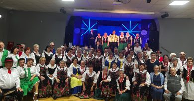 Ponad 120 osób w różnym wieku w strojach ludowych na tle sceny.