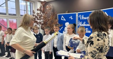 Kobieta z symbolicznym piórem pasuje najmłodszych uczniów szkoły. Uroczystość odbywa się w sali artystycznej.