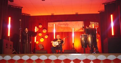 Oświetlona scena, a na niej artyści z instrumentami.