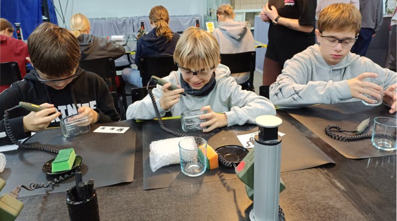 Trzech chłopców siedzących przy stołach rzemieślniczych, tworzących szklane gadżety.