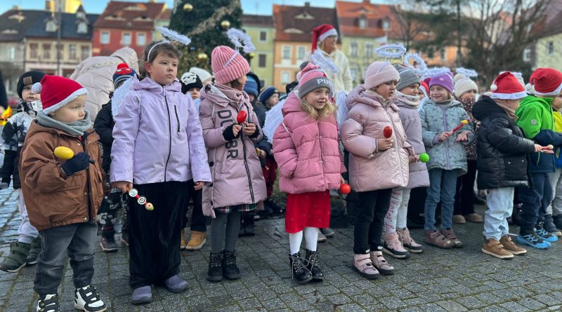 Grupa dzieci przedszkolnych, stojąca przy choince miejskiej.