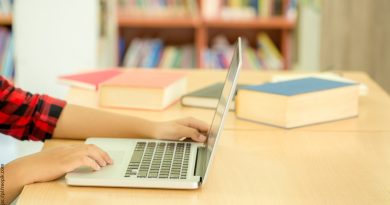 Ręka dziecka siedzącego w bibliotece przy laptopie.