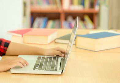 Ręka dziecka siedzącego w bibliotece przy laptopie.
