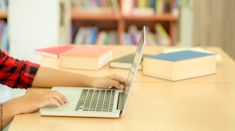 Ręka dziecka siedzącego w bibliotece przy laptopie.