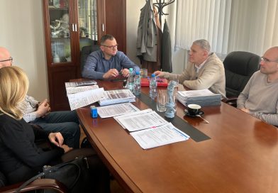 Pięć osób siedzących przy stole w gabinecie, na którym rozłożone są dokumenty.