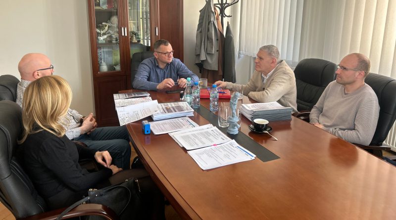 Pięć osób siedzących przy stole w gabinecie, na którym rozłożone są dokumenty.