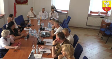 11 osób na sali siedzących na sali posiedzeń przy stole ułożonym w prostokąt.
